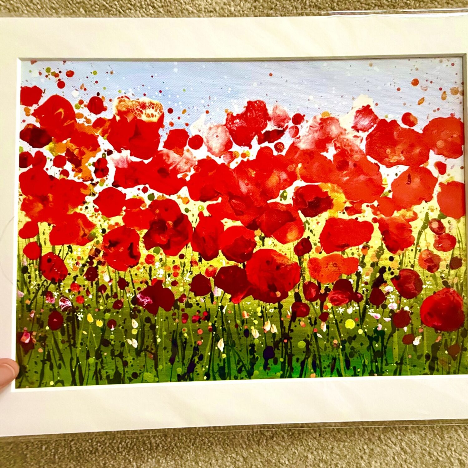 A Hand Holding The Ruby Days A3 Mounted Print, Showing Its White Mount Around A Colourful Red Poppy Meadow Scene.